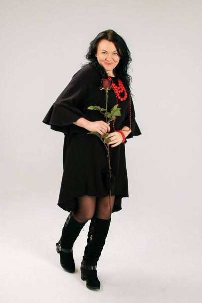 Atraktivní žena středního věku s červené růže taneční Studio v černých šatech a etnické náhrdelník - Fotografie, Obrázek
