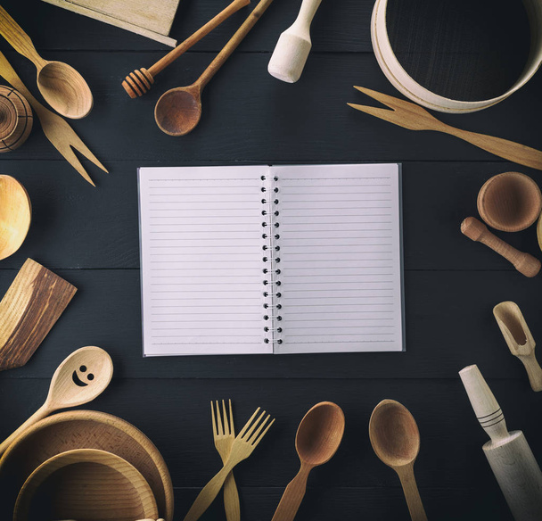 open notebook in a line on a black table in the middle of a wooden kitchen utensils, top view - Valokuva, kuva