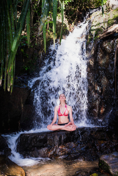 junge Frau praktiziert Yoga-Meditation unter Wasserfall - Foto, Bild