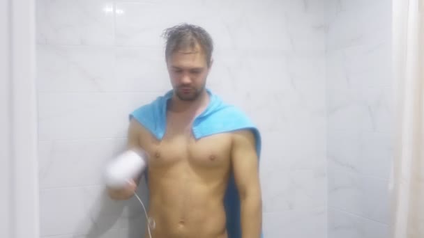 young handsome muscular man after shower in the bathroom. He put on a towel on his shoulders, portraying a superman, and blowing himself a blow dryer. 4k - Video, Çekim