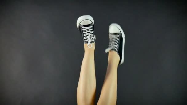 Naispuoliset jalat Classic Black and White Sneakers. Jalat on nostettu ylöspäin ja Dangle puolelta toiselle. Musta tausta. Klassiset kengät. Terveet elämäntavat
 - Materiaali, video