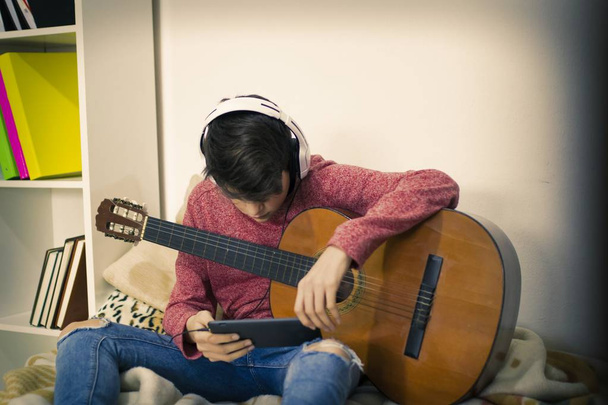 jovem tocando guitarra com fones de ouvido em casa
 - Foto, Imagem