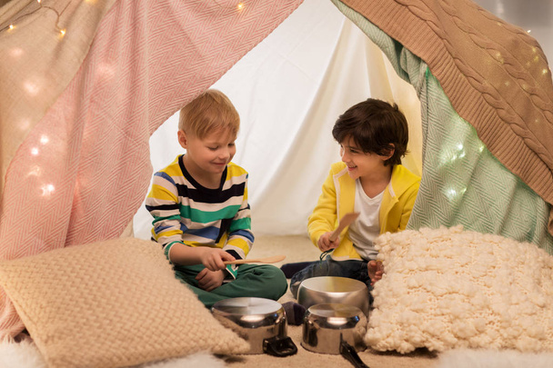 boys with pots playing music in kids tent at home - Фото, изображение