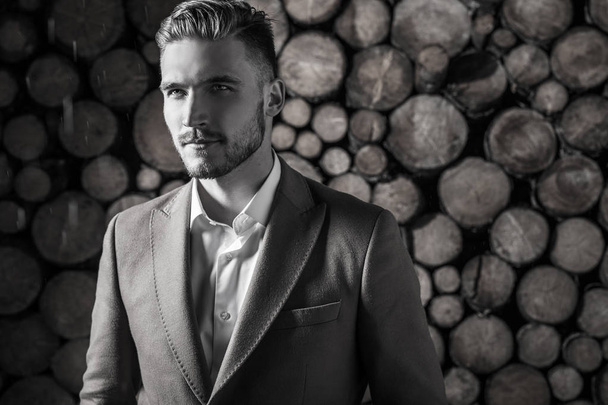Portrait of young beautiful fashionable man in coat against wooden background. Black-white portrait. - Fotografie, Obrázek
