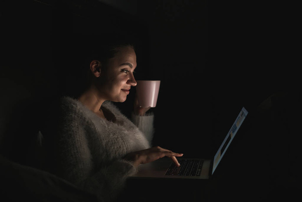 smiling young girl sitting in bed late at night, watching funny series on her laptop - Foto, Bild