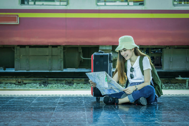 Aasia nainen Matkustaja istuu ja katselee karttaa ennen kuin matkustat rautatieasemalle, Matkailu ja elämäntapa konsepti
 - Valokuva, kuva