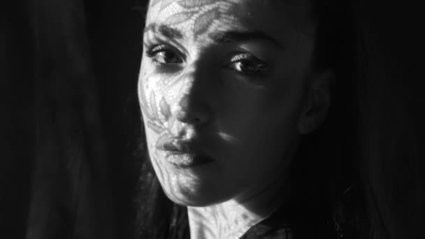 Beautiful woman's portrait with lace pattern shadow and sun light on her face / Beautiful woman looking through the window, she has got lace curtain pattern shadow and sun rays on her face - black and white video in slow motion - Footage, Video