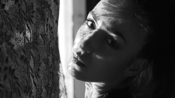 schöne Frauenporträt mit Spitzenmuster Schatten und Sonnenlicht auf ihrem Gesicht / schöne Frau schaut aus dem Fenster, sie hat Schatten und Sonnenstrahlen auf ihrem Gesicht - Schwarz-Weiß-Video in Zeitlupe - Filmmaterial, Video
