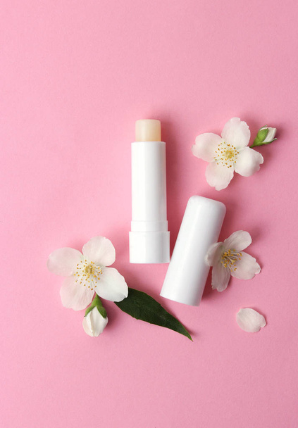 lippenbalsem en bloemen op een gekleurde achtergrond. minimalisme, de top - Foto, afbeelding