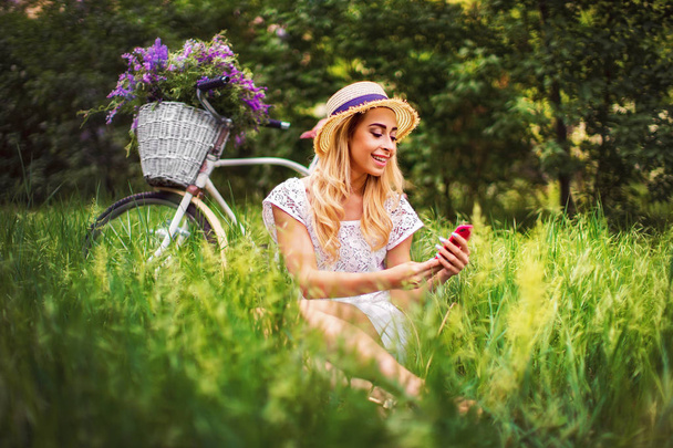 όμορφη νεαρή κοπέλα με vintage ποδηλάτων και άνθη σε φόντο πόλης στο φως του ήλιου υπαίθρια. - Φωτογραφία, εικόνα