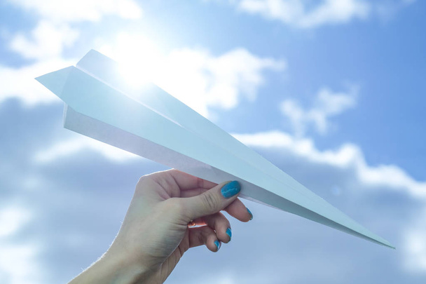 Hand hält Papierflugzeug über blauem Himmel mit Wolken.  - Foto, Bild