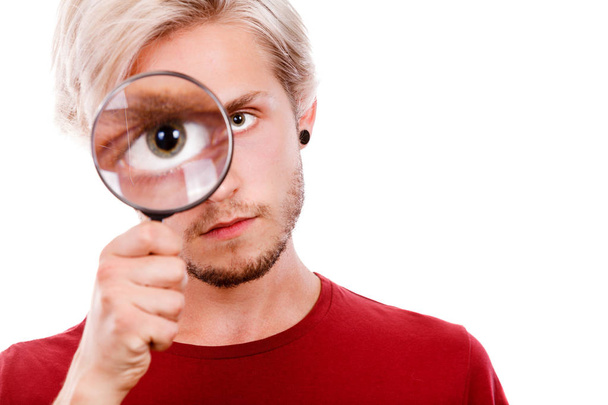Investigation exploration education concept. Young guy holding on eye magnifying glass looking through loupe, isolated on white - Φωτογραφία, εικόνα