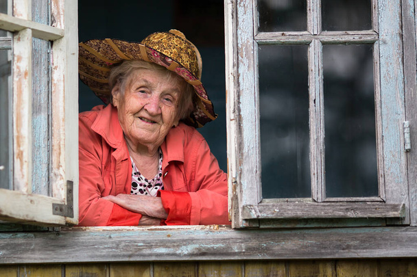 Starší žena v slaměný klobouk při pohledu z okna na farmě. - Fotografie, Obrázek