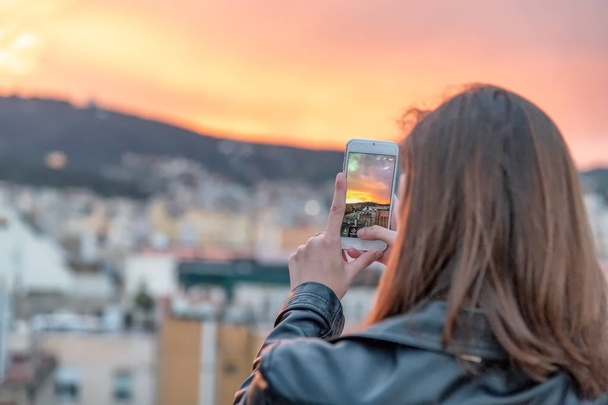 Back view of woman taking pictures of beautiful city sunset. - Photo, Image