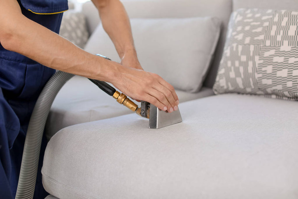 Dry cleaning worker removing dirt from sofa indoors - Foto, Imagen
