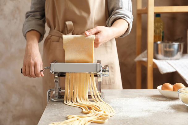 Young woman preparing noodles with pasta maker at table - Valokuva, kuva