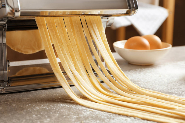 Pasta maker with dough on kitchen table - Valokuva, kuva