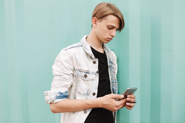 Portrait of young thoughtful man standing and using his cellphone on over blue background - Фото, зображення