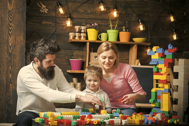 Father, mother and cute son play with constructor bricks. Kids playing with toys. Family on busy face spend time together in playroom. Educational game concept. Kid with parents play with plastic - Photo, Image