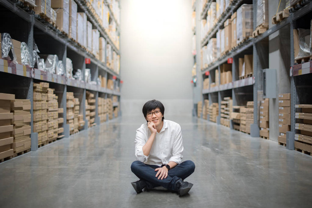 Молодой азиат, сидящий на складе, выбирая, что купить, концепцию складирования
 - Фото, изображение