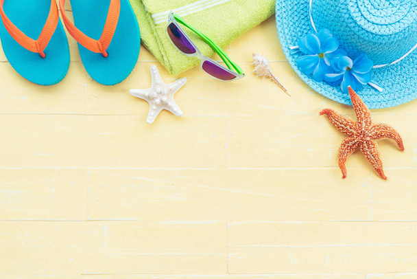 Akcesoria plażowe tym rozgwiazdy, plaży kapelusz, Okulary przeciwsłoneczne, zielony ręcznik, kolorowe przerzucania flop i muszli na jasny żółty pastelowe drewniane tła dla koncepcja lato urlop. - Zdjęcie, obraz