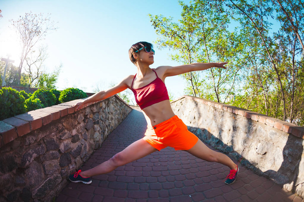 Een vrouw doet die zich uitstrekt in een stadspark. De opleiding van de ochtend in de natuur. Yoga praktijk. Fitness. Het meisje opwarmt voordat joggen. - Foto, afbeelding