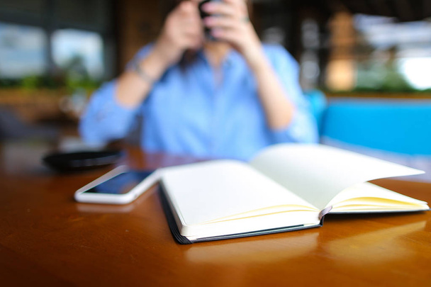 Close up diario vicino smartphone con ragazza al caffè in background, foto sfocata
. - Foto, immagini