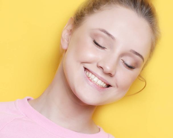 Jonge blonde vrouw met gesloten ogen, over gele achtergrond - Foto, afbeelding