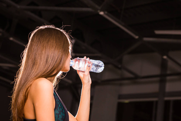 fitte junge Frau trinkt Wasser in der Turnhalle. muskulöse Frau macht Pause nach dem Sport - Foto, Bild