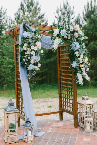 Floral arch with blue cloth and wooden elements at a rustic  wedding ceremony - Фото, зображення