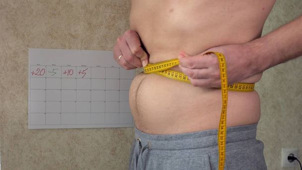 Lihava mies mittaa vyötäröään, isoa kaljavatsaansa, terveellistä elämäntapaansa
 - Valokuva, kuva