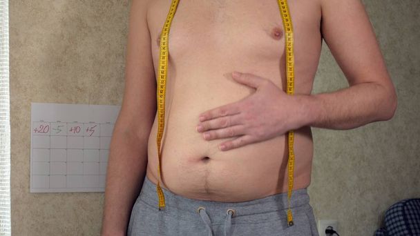 Um homem gordo mede a cintura, uma barriga de cerveja grande, um estilo de vida saudável pega dobras de gordura
 - Foto, Imagem
