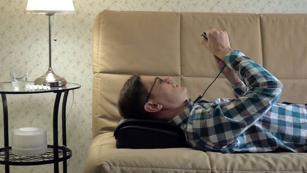 man lies on the couch at home, under the head of a massager, relaxed state - Φωτογραφία, εικόνα