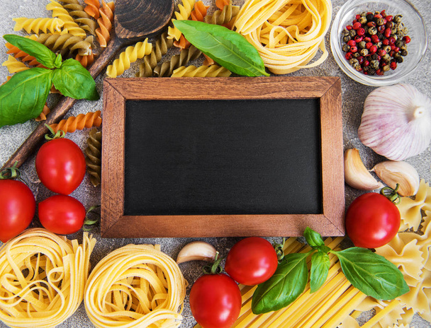 Italian food ingredients, pasta, tomatoes and blackboard on a stone background - Zdjęcie, obraz