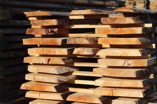 Grandes planches de bois empilées dans des racks pour sécher sous le ciel ouvert dans une zone industrielle. Timing du bois pour la menuiserie. Fabrication de meubles et d'articles en bois. Se débarrasser de l'humidité ligneuse
. - Photo, image
