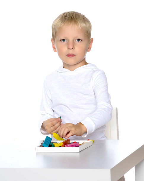 A cute little boy is sitting at a table and sculpting from plasticine. The concept of a happy childhood, learning and education of a child in a kindergarten. Isolated on white background. - Photo, image