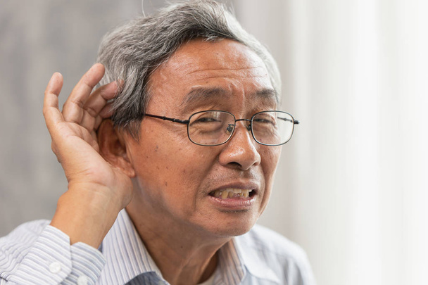 Asiático viejo hombre con sordo audición problemas lugar mano en oreja para ayudar a escuchar más fuerte
. - Foto, imagen