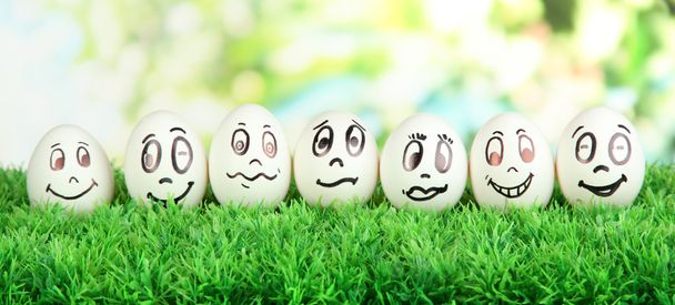Eggs with funny faces on grass on bright background - Fotó, kép