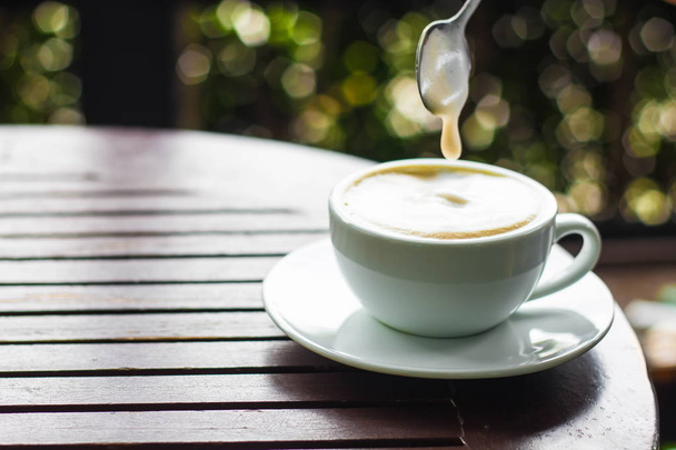 Beyaz fincan kahve kahverengi ahşap bir masa yerleştirilir ve bir adam elinde bir kahve bir kaşık ile yapıyoruz. - Fotoğraf, Görsel