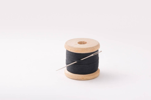 A wooden coil with threads of black color. The needle is threaded. - Foto, Imagem