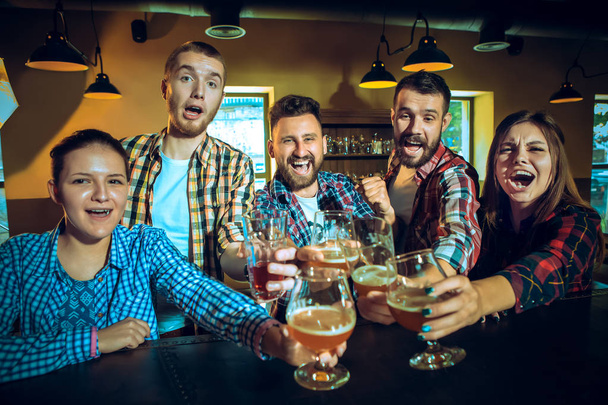 Sport, people, leisure, friendship and entertainment concept - happy football fans or male friends drinking beer and celebrating victory at bar or pub - Foto, imagen