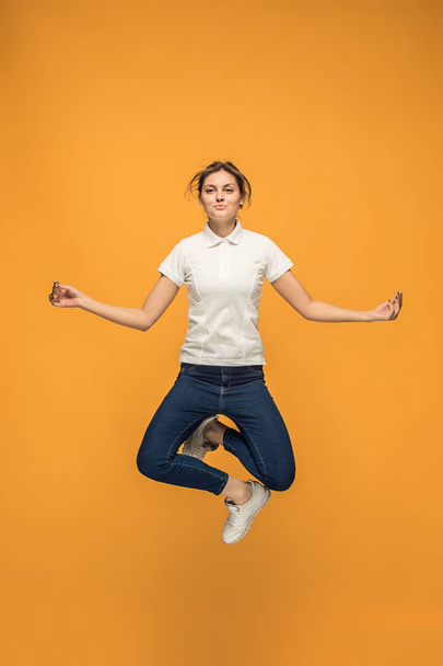 Freedom in moving. Pretty young woman jumping against orange background - Φωτογραφία, εικόνα