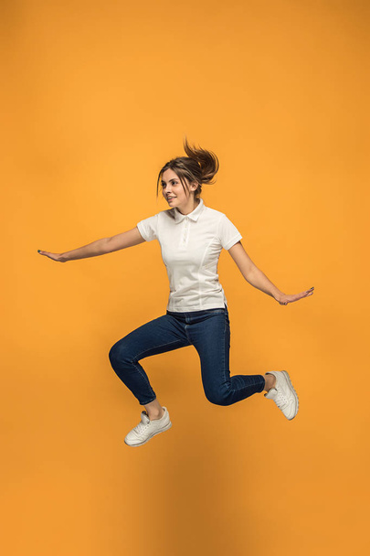 Freedom in moving. Pretty young woman jumping against orange background - Фото, зображення