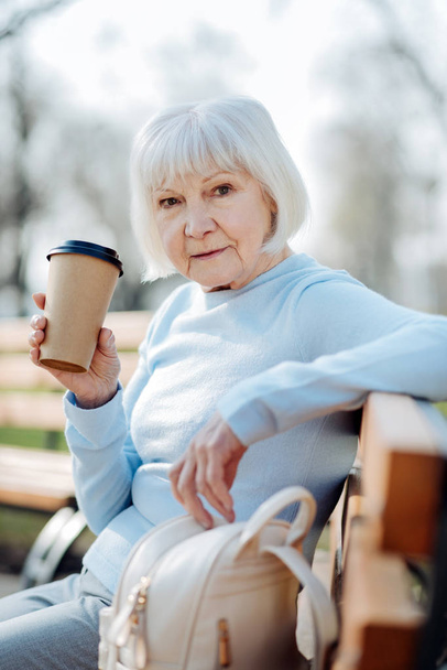 Koncentrált nő kávét iszik, miközben ül a padon - Fotó, kép