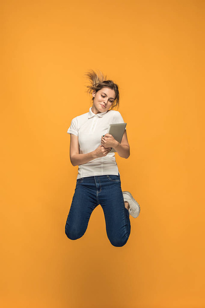 Image of young woman over orange background using laptop computer or tablet gadget while jumping. - Foto, immagini