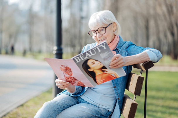 Exuberant aged woman reading a magazine - Фото, изображение