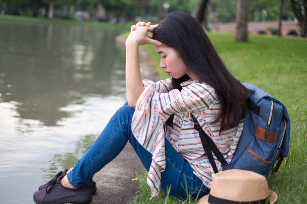 Aziatische vrouw backpacker er toeristen is stress en vermoeidheid. Ze heeft een verdriet. tijdens de reis. aan de waterkant openbaar park. in de vakantie en ontspannen. - Foto, afbeelding