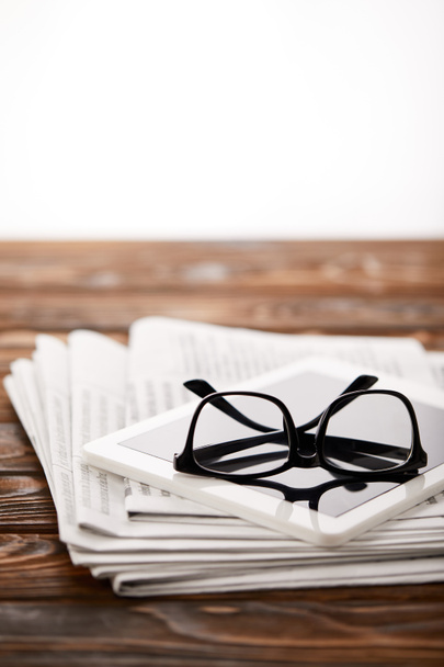 eyeglasses, digital tablet and pile of newspapers, on wooden background - Photo, Image