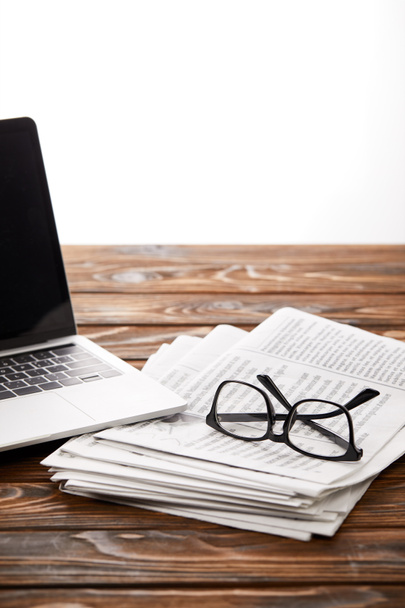 silmälasit kasa sanomalehtiä ja kannettava tietokone puupöydällä, valkoinen
 - Valokuva, kuva