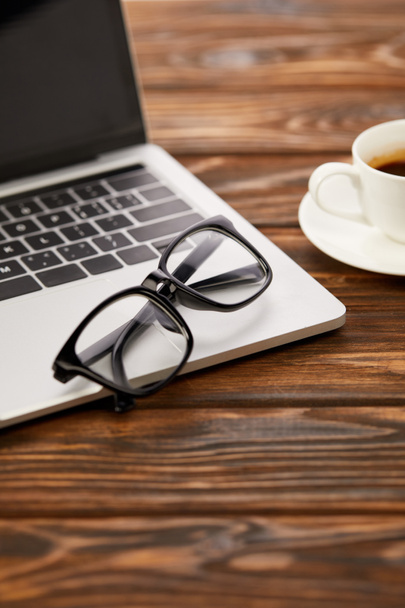 laptop, eyeglasses and cup of coffee on wooden table - Foto, imagen